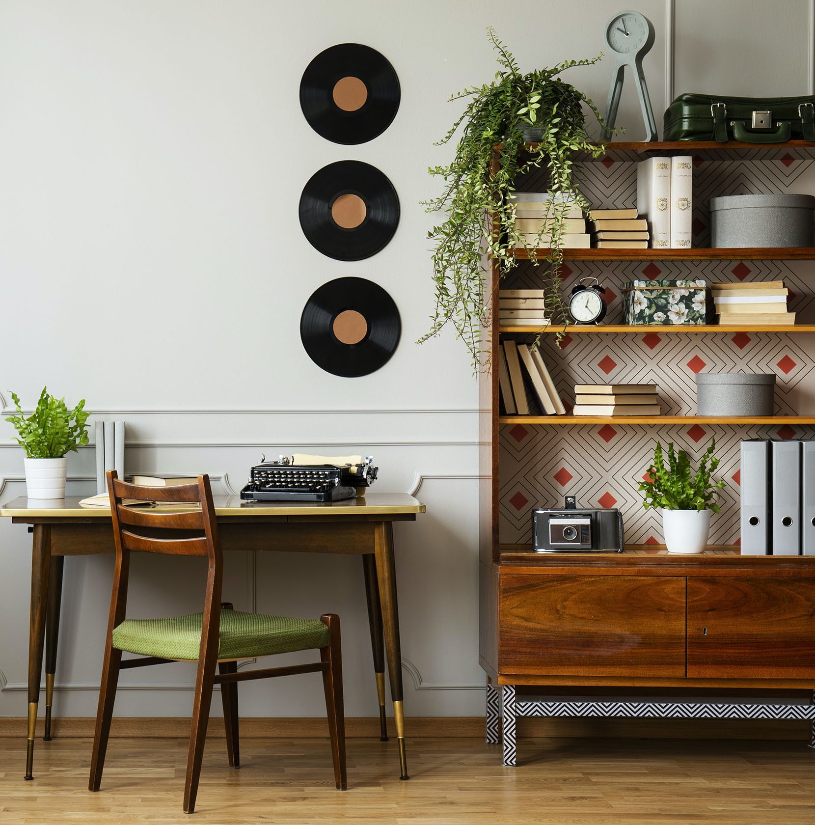 Black retro typewriter on a unique wooden desk, a mid-century modern chair and a renovated bookcase in a hipster home office interior. Real photo.